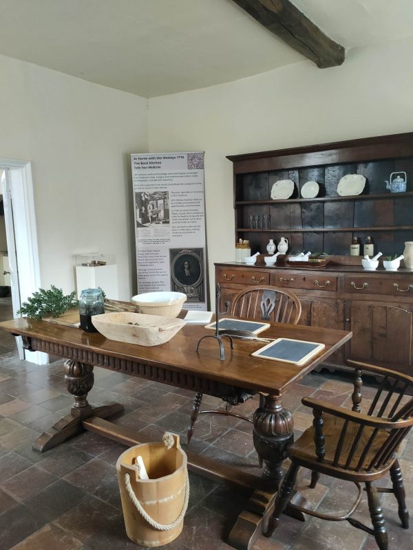 What would have been the back kitchen at Epworth Old Rectory featuring a long table, chairs and dresser with kitchen appliances and crockery.