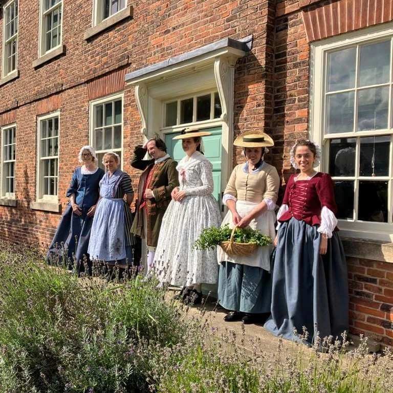 People dressed in 18th century clothes standing outside Epworth Old Rectory building.